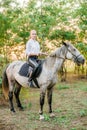 Beautiful young girl with light hair in uniform competition smiling and astride a horse in sunset