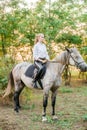 Beautiful young girl with light hair in uniform competition smiling and astride a horse in sunset