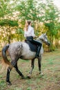 Beautiful young girl with light hair in uniform competition smiling and astride a horse in sunset