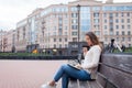 A beautiful young girl with long brown hair sitting on the bench with book and biting glasses while reading. She left the house on