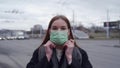 Beautiful young girl with long hair dresses a medical green mask on the street. Orvi, coronovirus, flu, acute