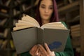 Beautiful young girl with long hair reads a book in the library Royalty Free Stock Photo