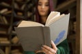 Beautiful young girl with long hair reads a book in the library Royalty Free Stock Photo