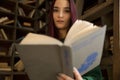 Beautiful young girl with long hair reads a book in the library Royalty Free Stock Photo