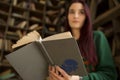 Beautiful young girl with long hair reads a book in the library Royalty Free Stock Photo