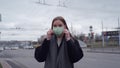 Beautiful young girl with long hair straightens a medical green mask against the background of passing cars. Orvi