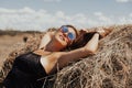 Beautiful young girl with long hair in sunnglasses posing on a wheat field near hay bales