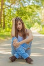 Beautiful young girl with long hair wearing jeans and a white t-shirt sitting on the road in the woods bright Sunny summer day Royalty Free Stock Photo