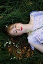 Beautiful young girl with long red curly hair. Girl with closed eyes lies on the green grass. view from above. Royalty Free Stock Photo