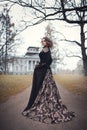 Beautiful young girl in a long vintage dress standing against the background of an old manor.