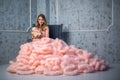 Beautiful young girl with long wavy hair holding a bouquet of flowers in pink dress-the-cloud watching is sitting on Royalty Free Stock Photo