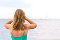 Blonde woman with long haircut in bright dress stands on ocean and looks into distance at ships. Back view Royalty Free Stock Photo