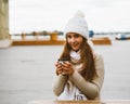 Beautiful young girl looking at camera, holding coffee, tea in reusable plastic mug in autumn, winter. A woman in warm clothes Royalty Free Stock Photo