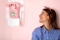 A beautiful young girl is looking at a retro looking telephone hanging on the wall in a pastry shop while eagerly awaits for a Royalty Free Stock Photo