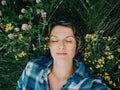 Beautiful young girl lying sleeping in grass among summer flowers nature outdoor. Pretty middle age woman lying dreaming on ground Royalty Free Stock Photo