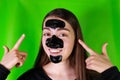 Beautiful young girl makes a black face mask from black dots on a green background on chromakey.