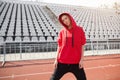 A beautiful young girl of mixed race stands on a sports stadium running track dressed in a red hoodie with a hood. Royalty Free Stock Photo