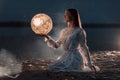 Beautiful young girl on a night beach with sand and stars holds the moon in her hands Royalty Free Stock Photo