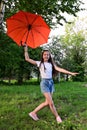 beautiful young girl with an orange umbrella is having fun on sunny summer day outdoors against the background of green foliage, Royalty Free Stock Photo