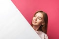 Beautiful young girl peeking out from behind white paper wall, on rose background Royalty Free Stock Photo