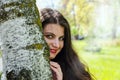 Beautiful young girl peeks out from behind a tree. Close-up plan. Sunbeams, summer day in the park.