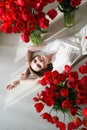 A beautiful young girl in a peignoir is lying on the floor between large bouquets of tulips. March 8 concept.