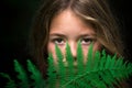 Beautiful young girl with perfect skin posing behind green fern in front black background. Teen model with brown hair. Spa Royalty Free Stock Photo