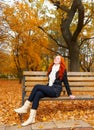 Beautiful young girl portrait sit on bench in park and relax, yellow leaves at fall season, redhead, long hair Royalty Free Stock Photo