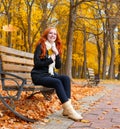 Beautiful young girl portrait sit on bench in park with yellow leaf in hand, fall season, redhead, long hair Royalty Free Stock Photo