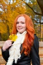 Beautiful young girl portrait sit on bench in park with yellow leaf in hand, fall season, redhead, long hair Royalty Free Stock Photo