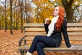 Beautiful young girl portrait sit on bench in park with yellow leaf in hand, fall season, redhead, long hair Royalty Free Stock Photo