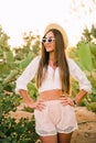 Young girl in hat and sunglasses posing against cactuses Royalty Free Stock Photo