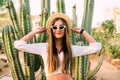 Young girl in hat and sunglasses posing against cactuses Royalty Free Stock Photo