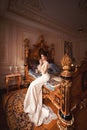 A beautiful young girl in a powdery wedding dress on the background of the interiors of a luxurious historical apartment.