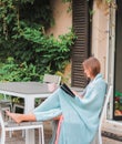 Beautiful young girl reading book with cup of tea outside in autumn garden wrapped into warm knitted blanket. Royalty Free Stock Photo