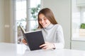 Beautiful young girl reading a book at home with a happy face standing and smiling with a confident smile showing teeth Royalty Free Stock Photo