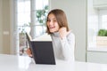 Beautiful young girl reading a book at home pointing and showing with thumb up to the side with happy face smiling Royalty Free Stock Photo