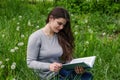 Beautiful young girl is reading a book while sitting in green grass. Royalty Free Stock Photo