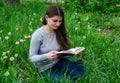 Beautiful young girl is reading a book while sitting in green grass. Royalty Free Stock Photo