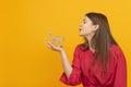 Beautiful young girl in red blouse holds grocery cart in palm of hand on bright orange background. Buyer or customer concept