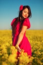 Beautiful young girl in a red dress posing in a field with canola. Happy woman on the nature. Spring season, warm day Royalty Free Stock Photo