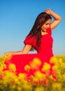 Beautiful young girl in a red dress posing in a field with canola. Happy woman on the nature. Spring season, warm day Royalty Free Stock Photo