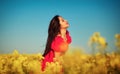 Beautiful young girl in a red dress posing in a field with canola. Happy woman on the nature. Spring season, warm day Royalty Free Stock Photo