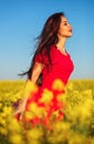 Beautiful young girl in a red dress posing in a field with canola. Happy woman on the nature. Spring season, warm day Royalty Free Stock Photo