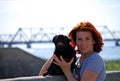 The beautiful young girl with red hair embraces on the street of the pet a black dog of breed a pug.