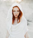 A beautiful young girl with red hair and freckles looks intently at the camera. Woman in the hood and clothes for the desert. Royalty Free Stock Photo