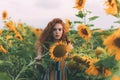 Beautiful young girl with red wavy hair and freckles in stripped colourful dress enjoying nature on the field of sunflowers. Royalty Free Stock Photo