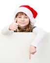 Beautiful young girl with santa hat standing behind white board. Royalty Free Stock Photo