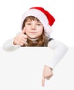 Beautiful young girl with santa hat standing behind white board. Royalty Free Stock Photo