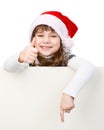 Beautiful young girl with santa hat standing behind white board on white Royalty Free Stock Photo